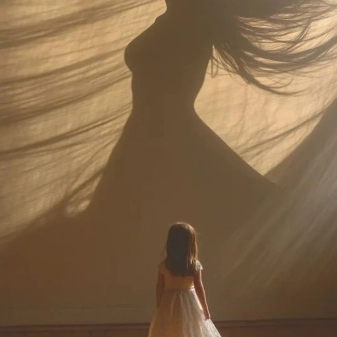 Una niña mira la sombra de una mujer proyectada en una tela, metáfora de la niña interior